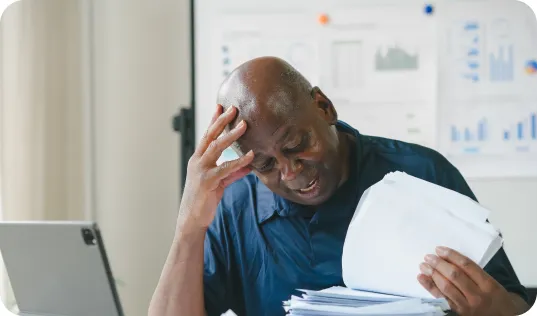 Man stressed reviewing paperwork with a tablet in front of him, hand on his forehead
